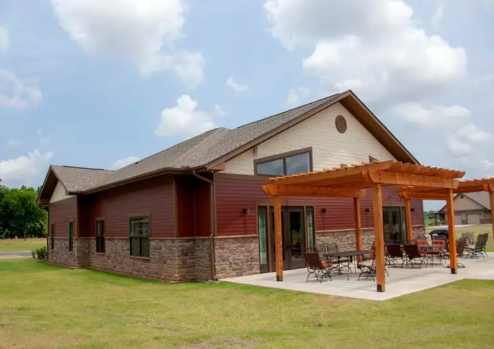 A community building with a shingle roof, red siding and a timber pergola