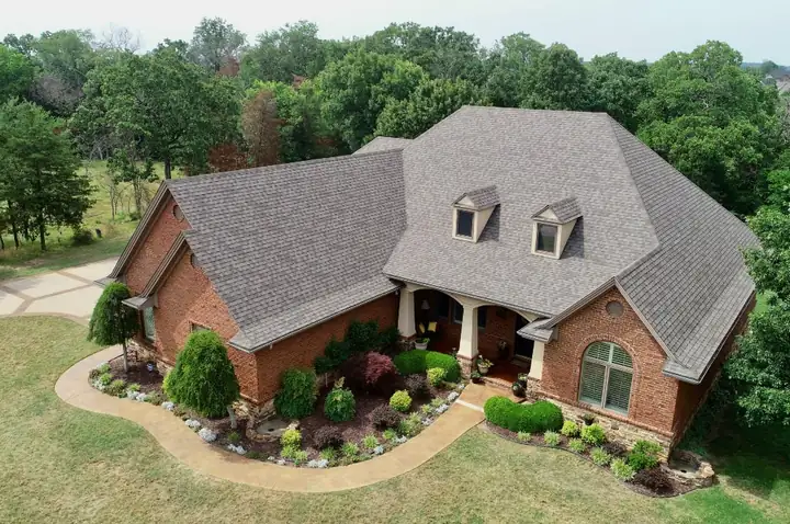 Drone view of a brick home with a finished shingle roof and two dormers