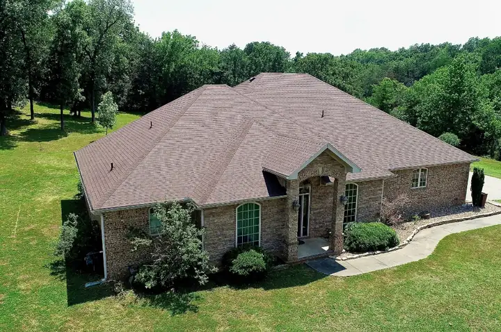 Drone view of a brick home in woodland with a finished brown shingle roof