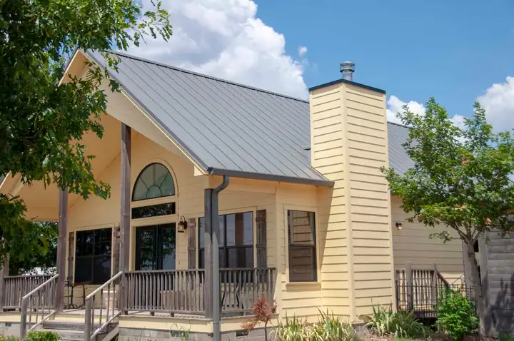 A yellow house with a finished grey standing seam metal roof