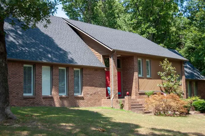 A brick ranch home with a finished dark shingle roof and a red front door