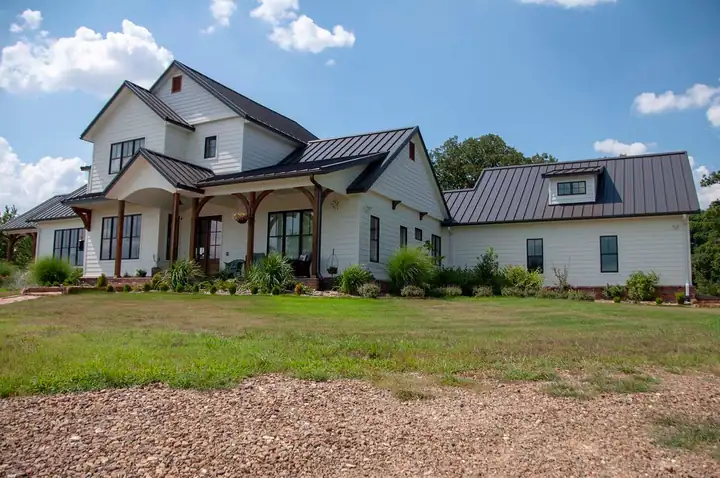 A white farmhouse with a finished dark standing seam metal roof