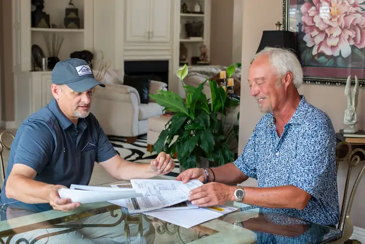 A Foster Roofing estimator going through paperwork with a homeowner at a glass table
