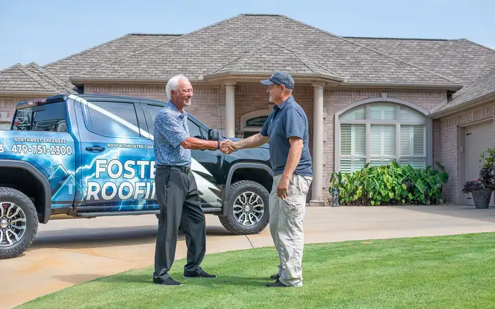 A Foster Roofing estimator shaking hands with a homeowner, with the company truck behind