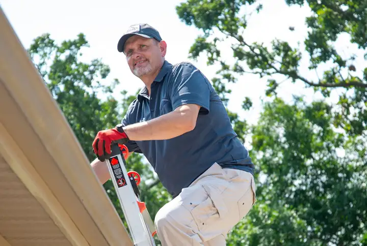 A Foster Roofing estimator at the top of a ladder looking across a roof